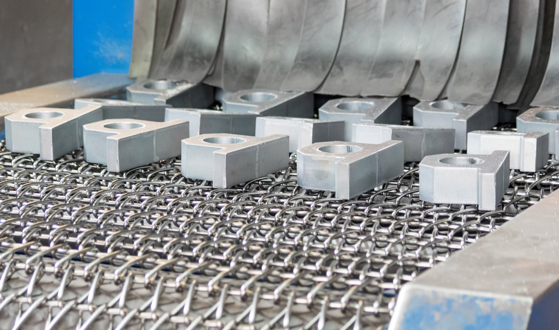 Metallblöcke mit runden Aussparungen auf Transportband von Maschine